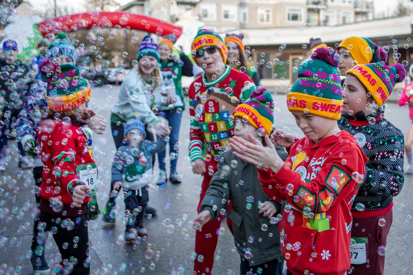 Children in Christmas sweaters and festive hats playing among bubbles